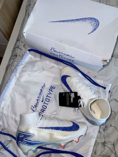 a pair of white and blue nike shoes next to a shoe box on a bed