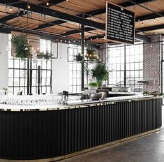 an empty restaurant with lots of windows and plants on the bar counter, along with hanging lights