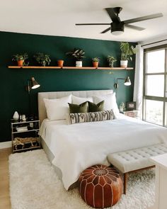 a bedroom with green walls, white bedding and potted plants on the wall