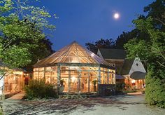 a glass house lit up at night with the moon in the sky above it and trees surrounding