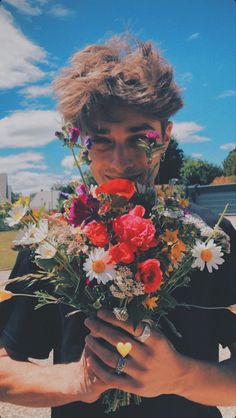 a young man holding a bouquet of flowers in his hands and looking at the camera