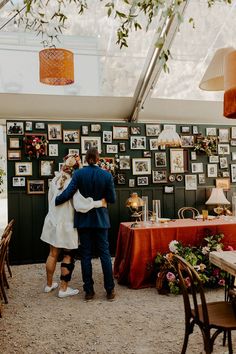 a man and woman embracing each other in front of a table with pictures on the wall