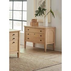 a wooden dresser sitting in front of a window next to a plant on top of a rug