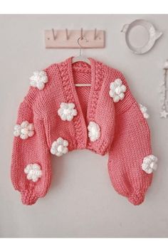 a pink knitted sweater with white flowers on it and a key hanging from the wall