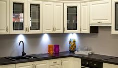 a kitchen with white cupboards and black counter tops is lit by recessed lights