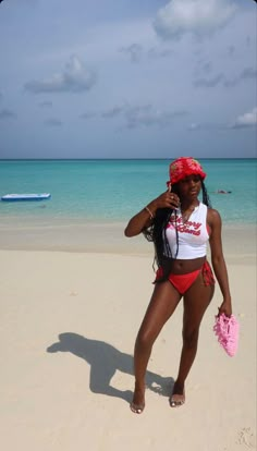 a woman standing on top of a sandy beach next to the ocean wearing a red and white bathing suit