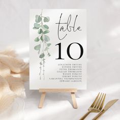 the table numbers are displayed on an easel with gold forks and napkins next to it