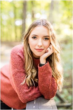 a beautiful young woman leaning on a bench smiling at the camera with her hand under her chin