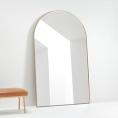 a mirror sitting on top of a white wall next to a bench and stool in front of it