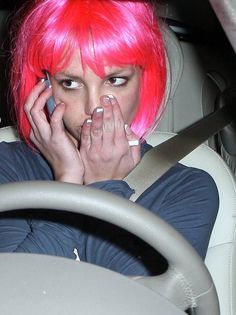 a woman with pink hair is talking on her cell phone in the back seat of a car