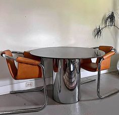 a round table with chairs around it in the middle of an empty room, next to a plant