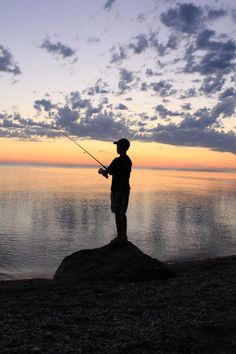 a man standing on top of a beach next to the ocean holding a fishing pole