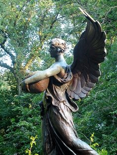 a statue with wings holding a basket in its hand and looking up at the sky