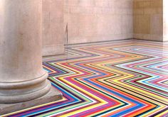 the floor is covered with multicolored lines and columns in an empty room that appears to be very colorful