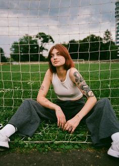 a woman sitting on the ground in front of a soccer net with her arms crossed