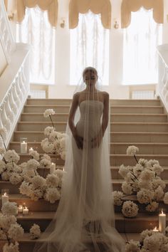 a woman in a wedding dress standing on some stairs with flowers and candles around her