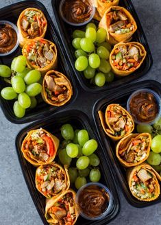 four black trays filled with different types of food and some grapes on the side