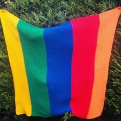 a rainbow colored blanket laying on top of a green grass covered ground next to bushes