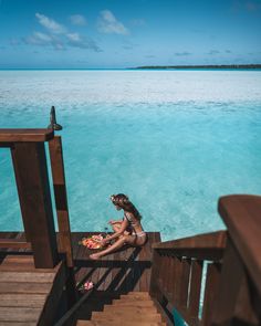 a woman sitting on top of a wooden staircase next to the ocean