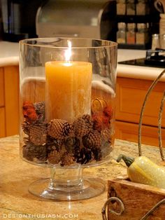 a candle is sitting in a glass bowl on a counter top with pine cones and acorns