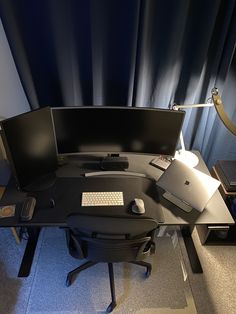 an office desk with a computer monitor, keyboard and mouse on it in front of a black curtain