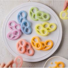 a white plate topped with lots of different colored plastic scissors next to a person's hand