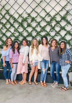 a group of women standing next to each other in front of a wall covered with greenery