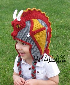 a young boy wearing a crocheted hat with horns on it sitting in the grass