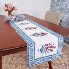 a table runner with blue and red flowers on it sitting on top of a wooden table