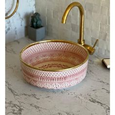 a pink and gold bowl sitting on top of a counter next to a faucet