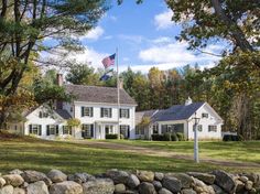 a large white house sitting on top of a lush green field next to a forest