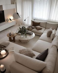 a living room filled with lots of white furniture and candles in front of a large window