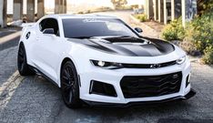 a white chevrolet camaro with black stripes on it's hood parked in the street