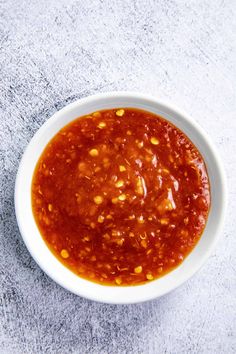 a white bowl filled with red sauce on top of a gray tablecloth covered floor