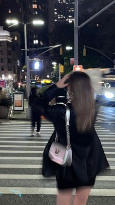 a woman is crossing the street at night with her hair blowing in the wind and wearing a black dress