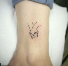 a small tattoo on the ankle of a woman's hand holding another person's hand