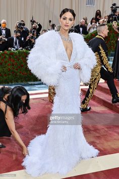 a woman in a white gown and feathered coat poses on the red carpet at the met