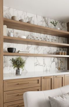 a white couch sitting in front of a wooden shelf filled with vases and bowls