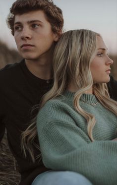 a young man and woman sitting next to each other on the ground looking off into the distance