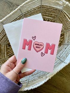 a woman holding up a pink card with the word mom on it and two hearts