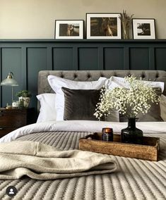 a bed with pillows and blankets on top of it next to a vase filled with baby's breath flowers