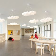 the children are sitting at the table in the room with clouds hanging from the ceiling