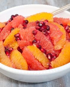 a white bowl filled with oranges and pomegranate