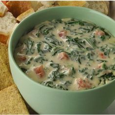 a green bowl filled with cheese and spinach next to some crackers on the side