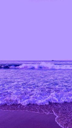 an ocean view with waves coming in to shore and purple hues on the sky