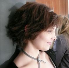 a woman with short hair wearing a black shirt and silver necklace looking out the window