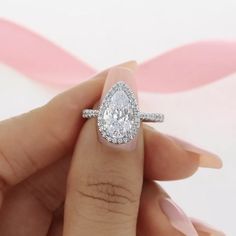 a woman's hand holding an engagement ring with a pear shaped diamond on it