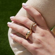 a woman's hand wearing a gold ring with diamonds on it and a green grass background