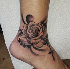 a black and white rose tattoo on the foot with rosary beads around it's ankles