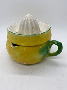 a yellow cup with a green handle and a white object in the middle, on a white surface